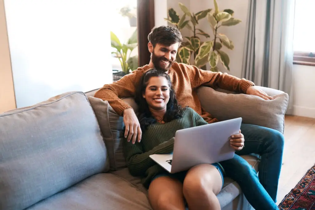 Couple relaxing on their sofa while one of them works on a laptop