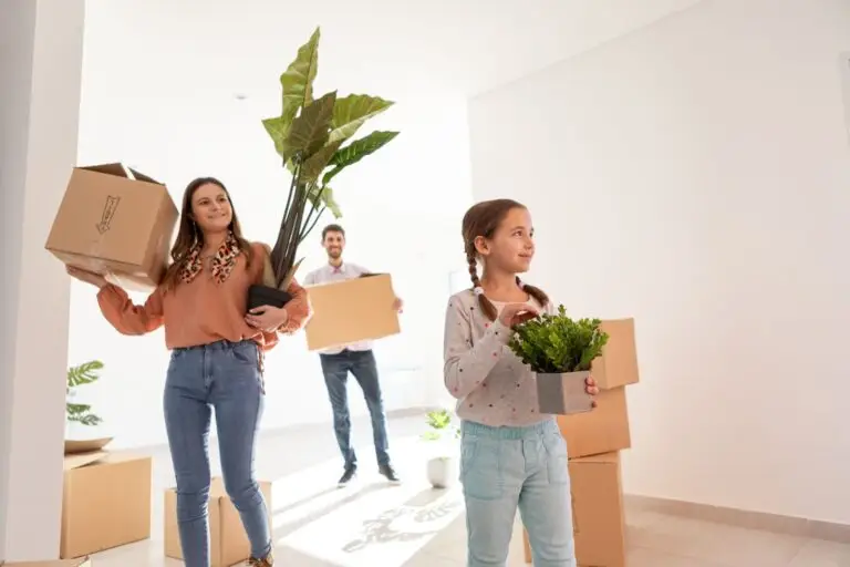 Family carrying moving boxes and potted plants into their new home