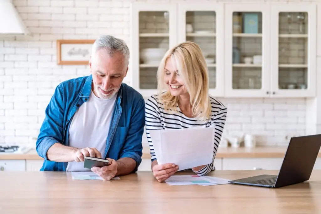 Couple at their kitchen table reviewing paperwork with a calculator