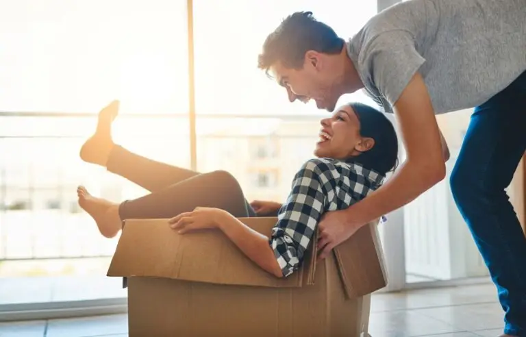 Man playfully pushing a laughing woman who sits inside a moving box