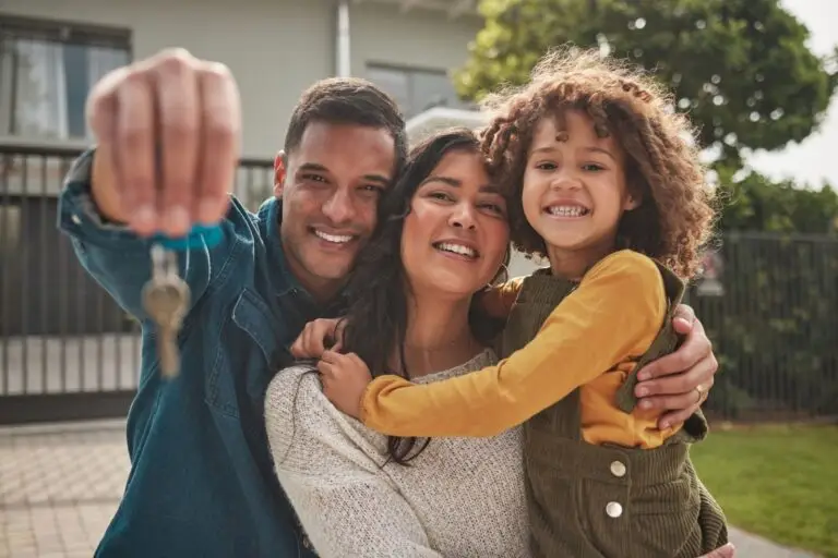 Family hugging outside their new home while holding up the keys