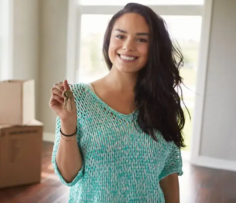 Smiling woman in a knit sweater holding up keys inside her new home