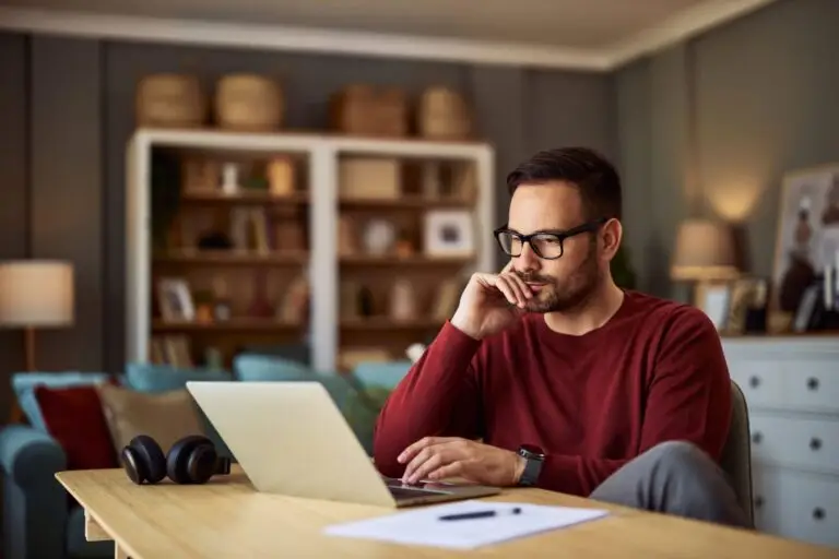 Man in glasses working on a laptop at a wooden table at home