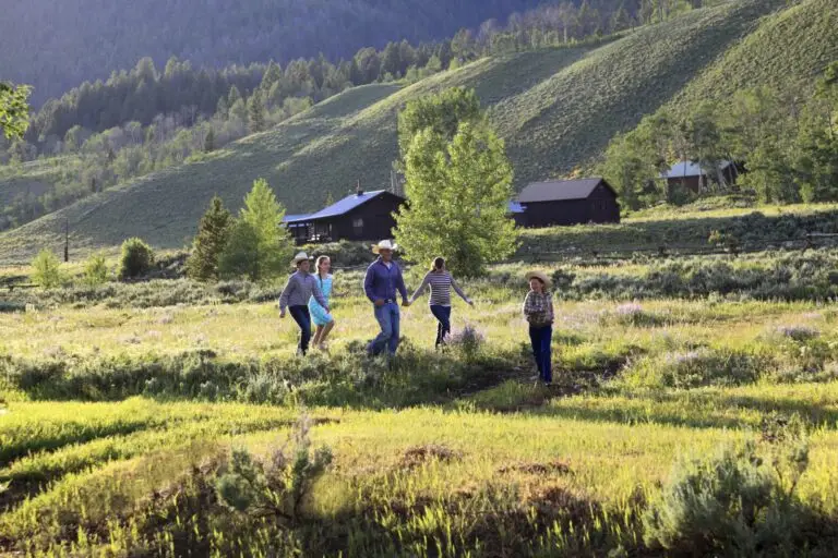 Family in cowboy hats running through a meadow below hillside log cabins