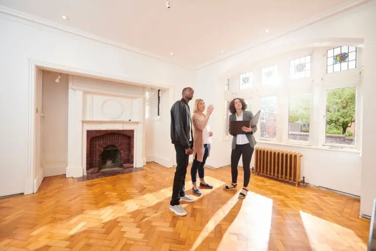Couple touring a bright empty room with a fireplace alongside an agent