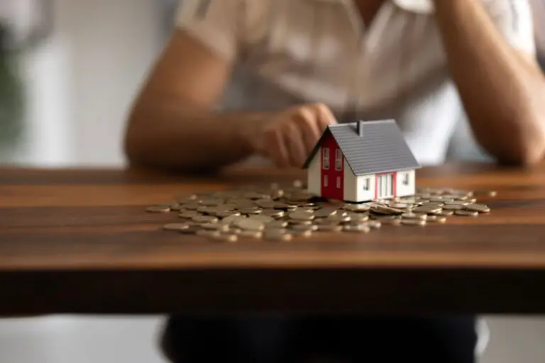 Small model house sitting on a pile of coins on a wooden table