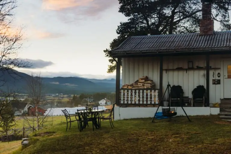 White country cottage with stacked firewood on the porch and mountain views