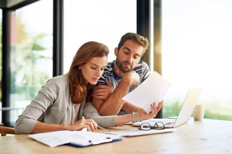 Couple reviewing paperwork together at a table beside a laptop