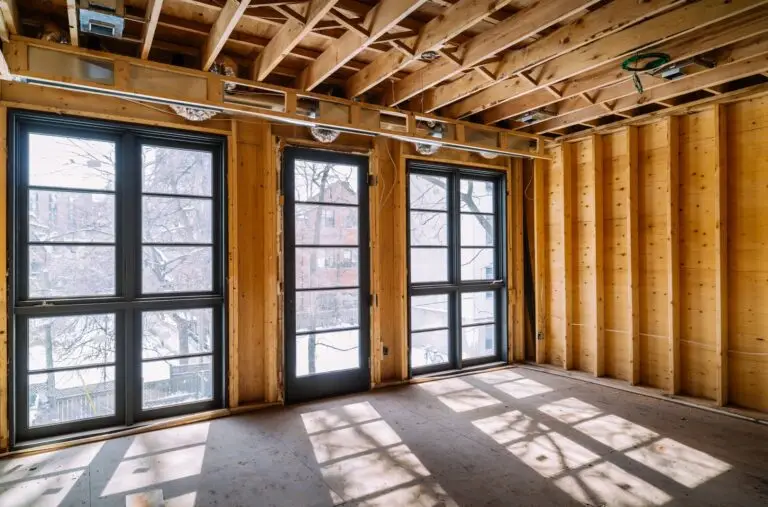 Unfinished interior with exposed wood framing and sunlight through tall windows