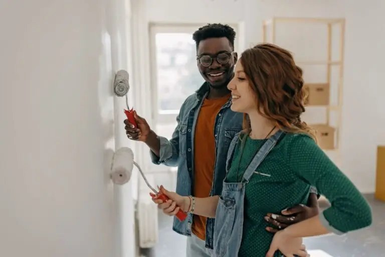 Smiling couple painting a white wall together with paint rollers