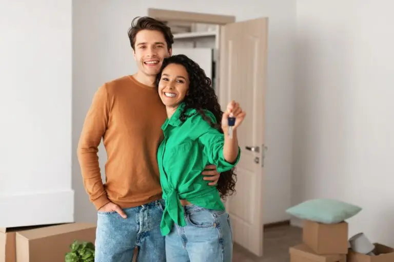 Smiling couple holding up a key beside moving boxes in their new home