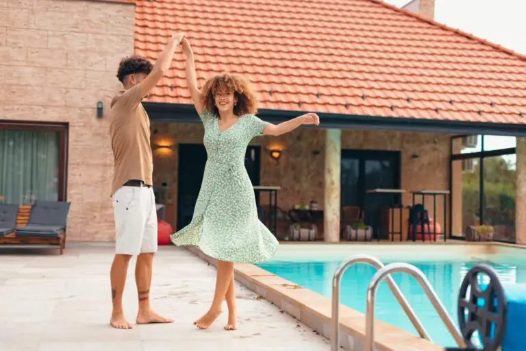 Couple dancing barefoot beside a backyard swimming pool at their home