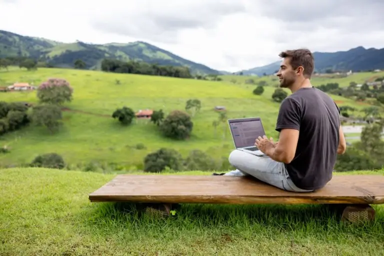 Man working on a laptop outdoors overlooking green rolling hills