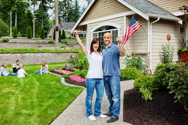 Couple cheering with house keys outside a home flying an American flag