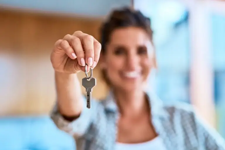 Smiling woman holding a single house key out toward the camera