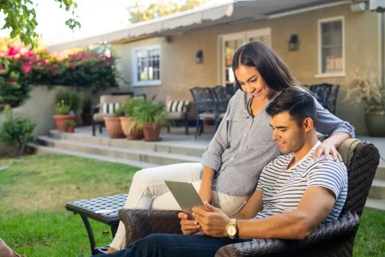 Couple relaxing on a patio chair and looking at a tablet in their backyard