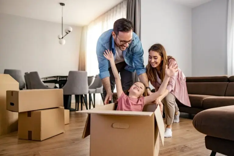 Parents laughing with their young daughter as she plays in a moving box