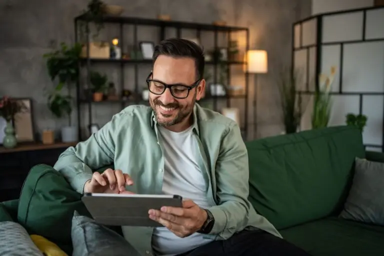 Smiling man in glasses using a tablet on a green sofa at home