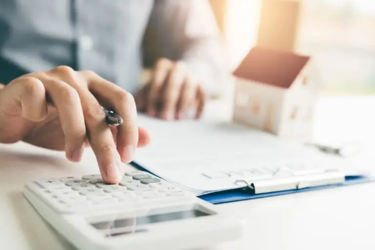 Hand using a calculator beside a small model house and paperwork