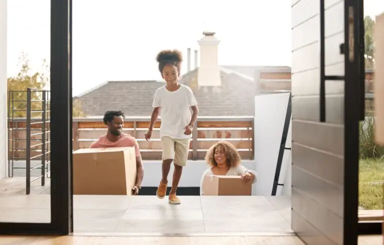 Family carrying moving boxes into their home as a child runs ahead