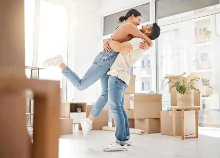 Woman leaping into her partner's arms in a new home full of moving boxes