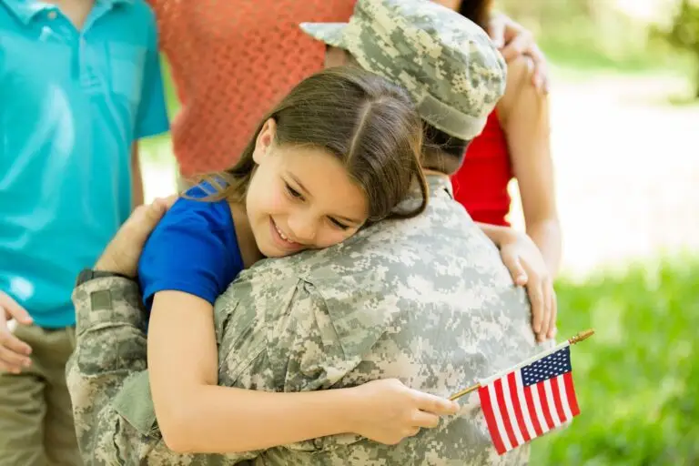 Young girl holding a small American flag while hugging a soldier in uniform