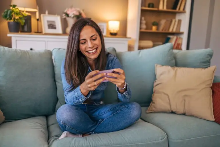 Smiling woman sitting cross legged on a sofa and looking at her phone