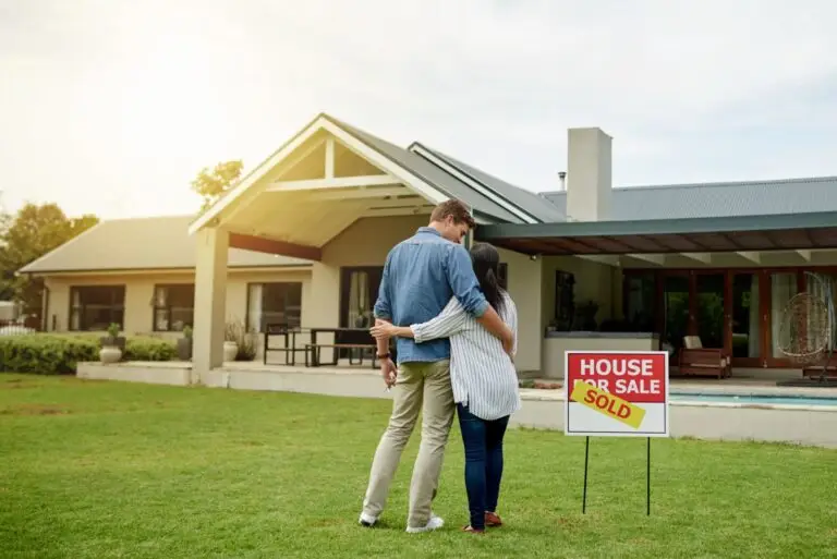 Couple embracing on the lawn beside a sold sign outside their new home