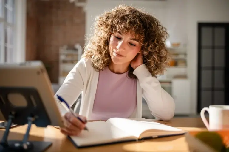 Woman with curly hair writing notes in a notebook at her desk