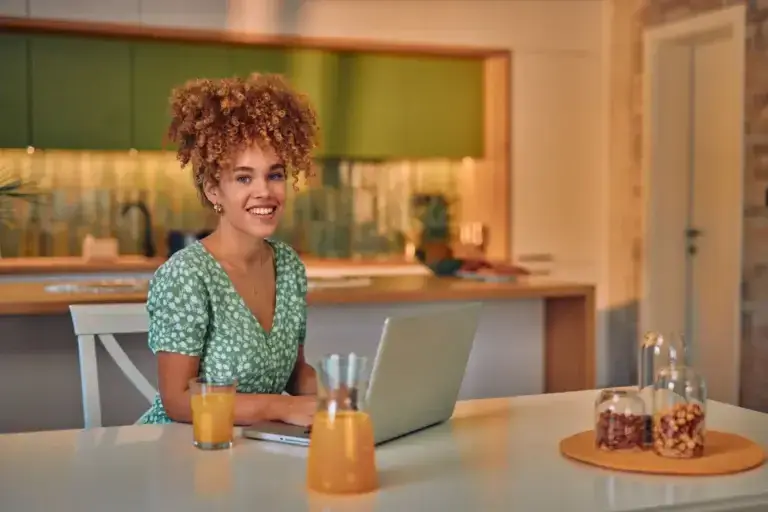 Smiling woman at a kitchen table with a laptop and orange juice