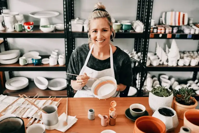 Smiling ceramic artist painting a bowl in her pottery studio