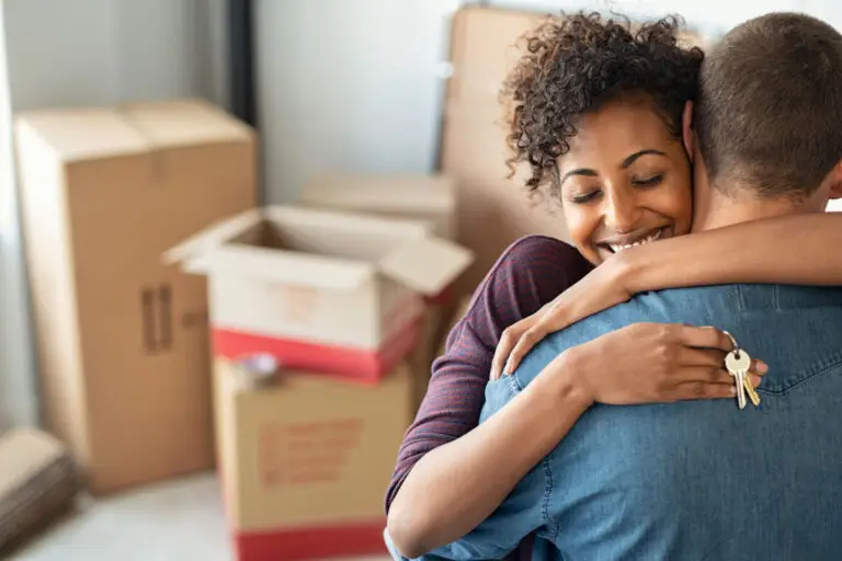 Woman hugging her partner while holding house keys beside moving boxes