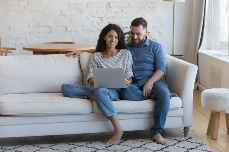 Couple relaxing together on a white sofa while looking at a laptop