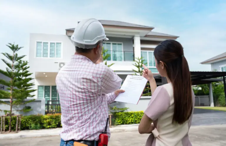 Builder in a hard hat showing a woman a document outside a large home