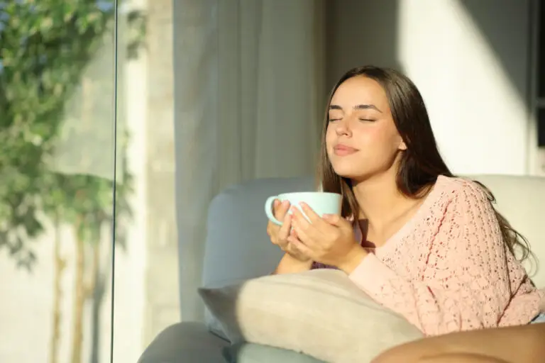 Woman with her eyes closed enjoying a cup of coffee in warm sunlight